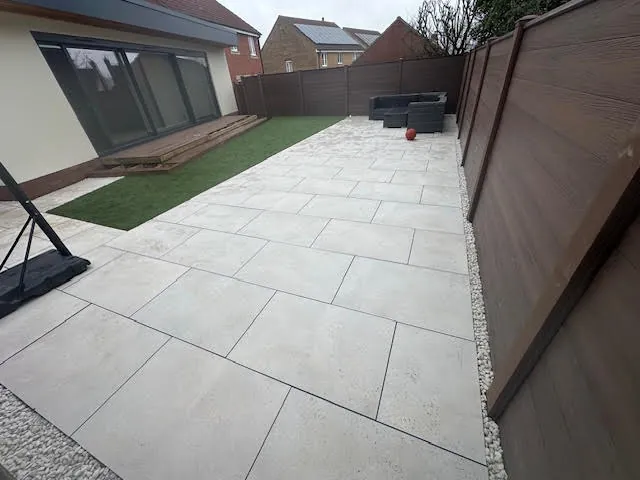 Large porcelain patio with artificial grass beside a garden room