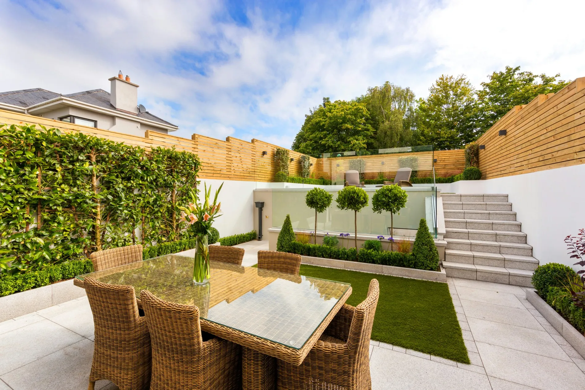 Porcelain patio with lawn, granite steps, slatted fencing and planting in a modern back garden